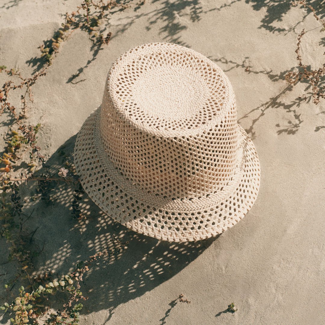 Beige bucket hat on sandy ground with sunlight and plant shadows.