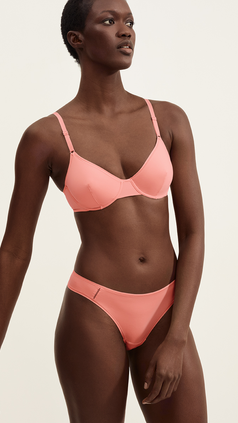 Frau tr&auml;gt ein pfirsichfarbenes BH- und Slip-Set mit verstellbaren Tr&auml;gern und minimalistischem Design.