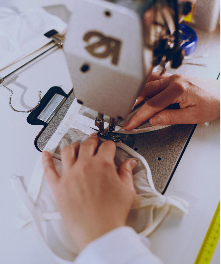 Close-up of hands guiding fabric through an industrial sewing machine, showcasing textile production, garment manufacturing, or tailoring work in progress.
