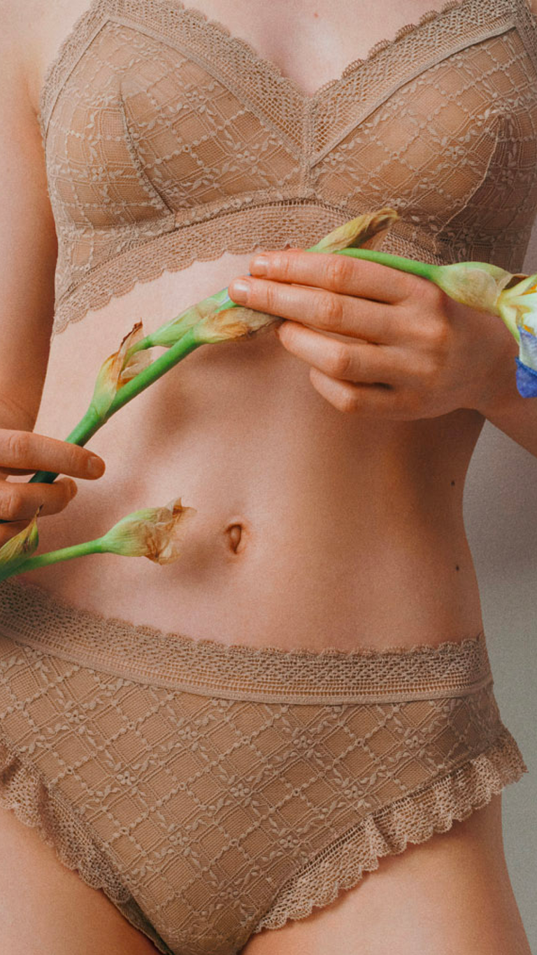 Una mujer lleva un sujetador de encaje beige y sostiene una flor entre sus manos.