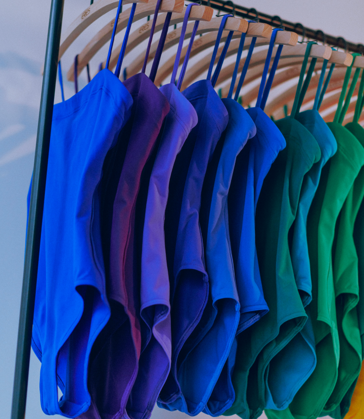 A vibrant gradient of blue and green swimsuits hanging on a retail rack, showcasing a colorful swimwear collection.