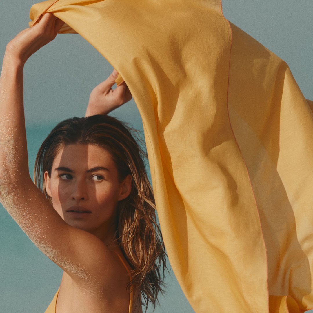 Woman holding a yellow pareo in the wind at the beach, summer vibes, sun and sea.