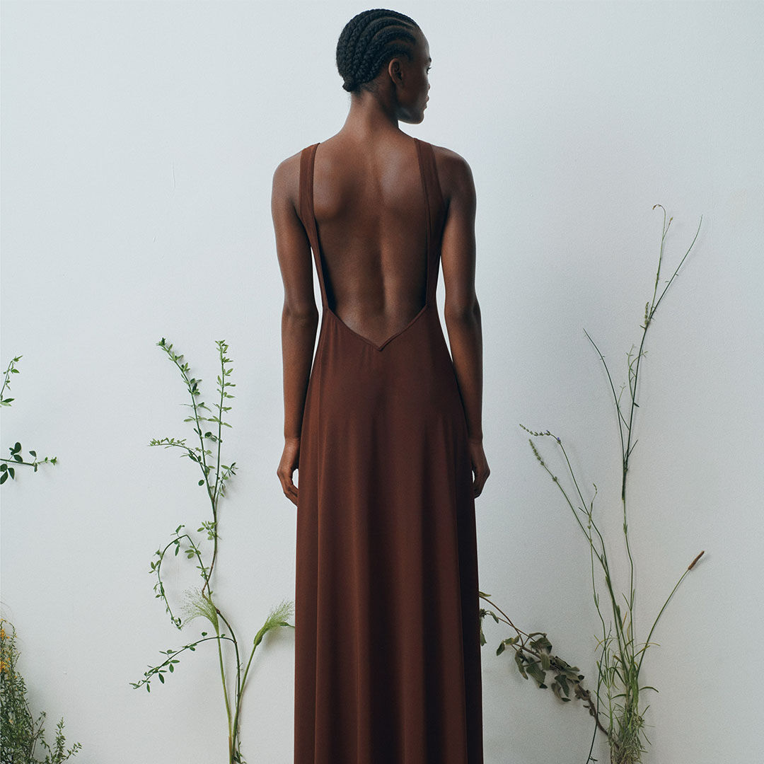 Woman in backless brown dress, standing.
