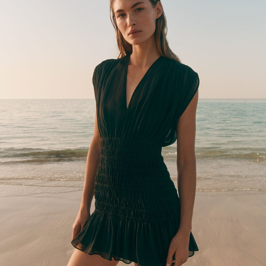 Mujer junto al mar con un vestido negro corto.