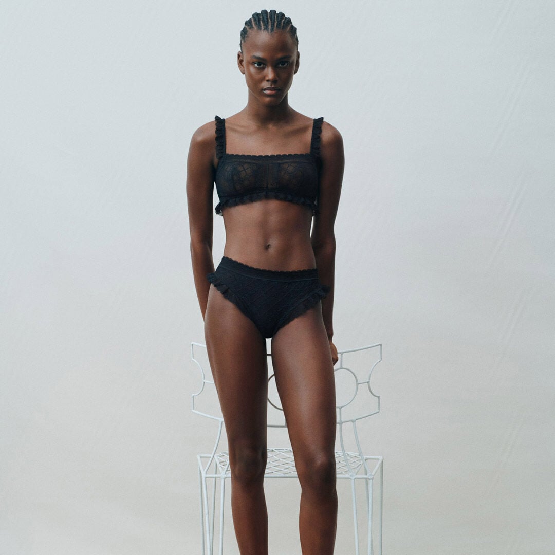 Model wearing a black lace lingerie set with ruffle details