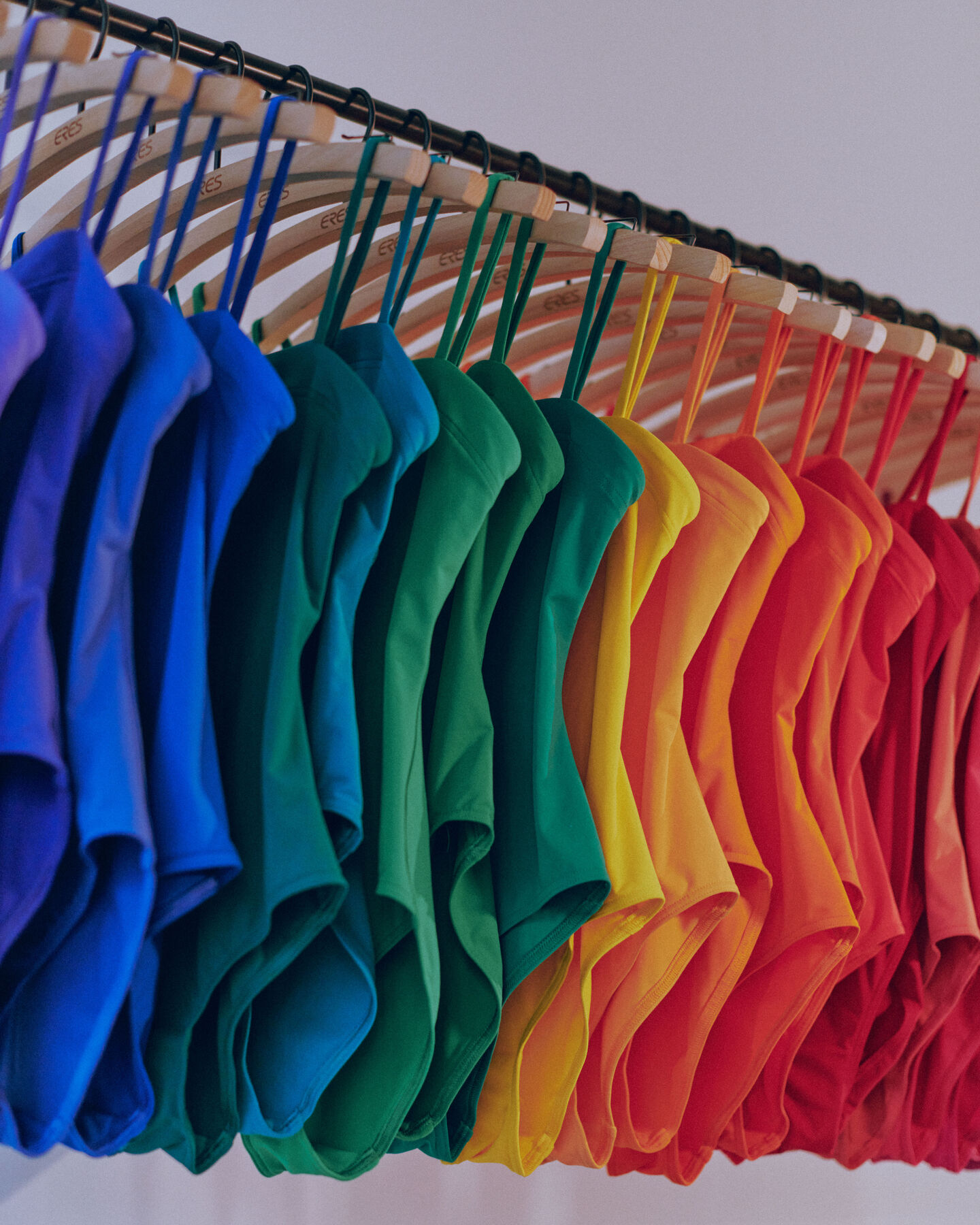 A vibrant gradient of blue and green swimsuits hanging on a retail rack, showcasing a colorful swimwear collection.