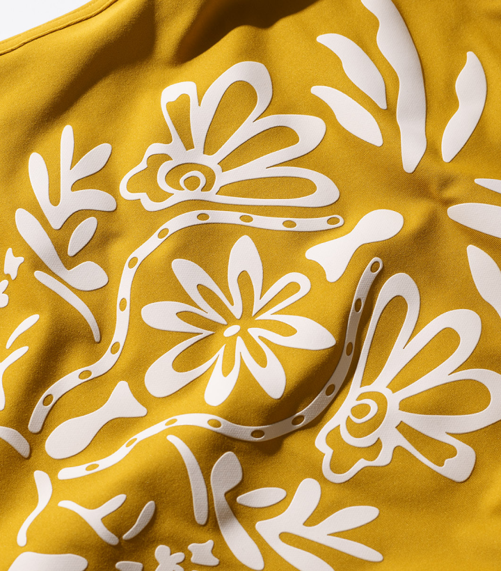 Wavy yellow fabric with a white decorative Maharajah-themed print featuring stylized flowers and dragonfly-like insects.