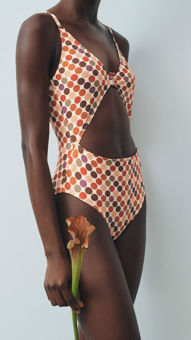 Mannequin in a retro polka dot cut-out one-piece swimsuit, holding an orange calla lily.