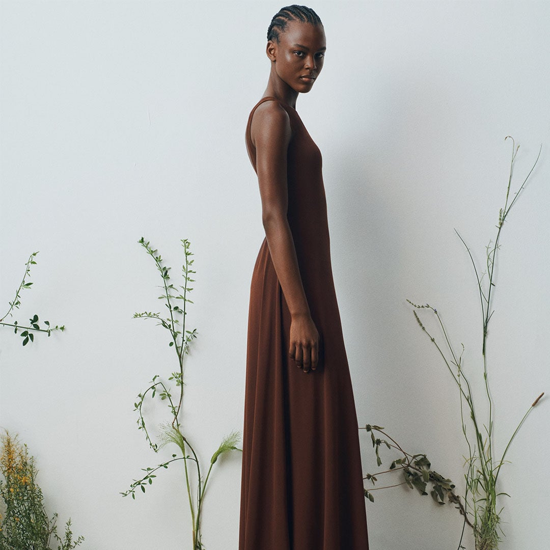 Woman in brown sleeveless dress, standing sideways.