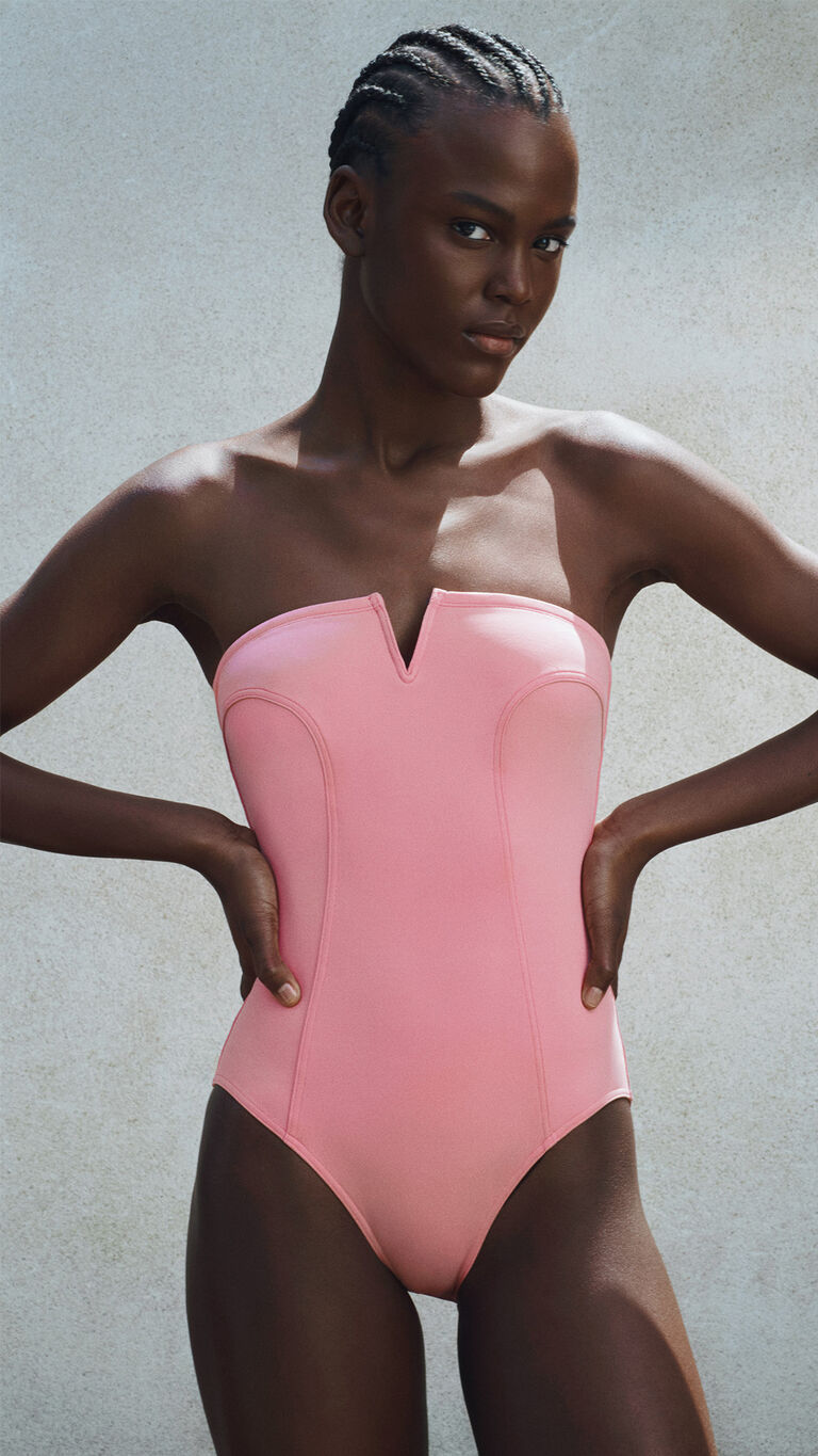 Woman wearing a pink bandeau one-piece swimsuit with a V-notch neckline and structured silhouette.